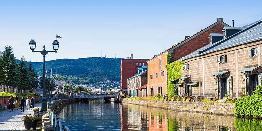 The Otaru Canal is lined with old fashioned brick buildings and warehouses on a bright day. 