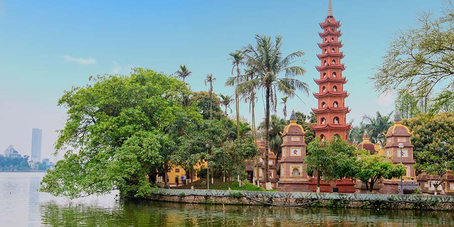 A traditional Vietnamese red pagoda stands tall on a small island surrounded by trees and other plant life. 